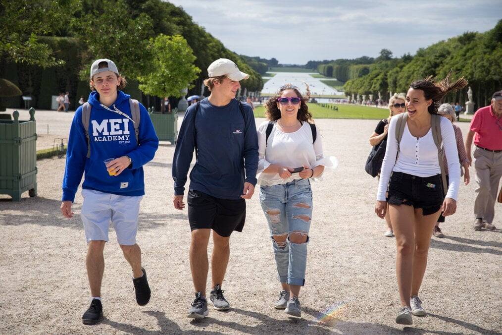 Four teens walk through a garden in France with backpacks on.