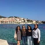 group of four students standing in front of the ocean with little building behind them