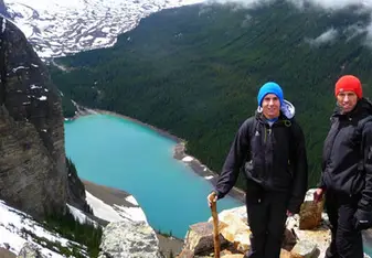 a girl stands on a ledge over looking a lake in the mountains