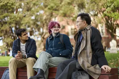 Three students smiling at eachother while sitting outside