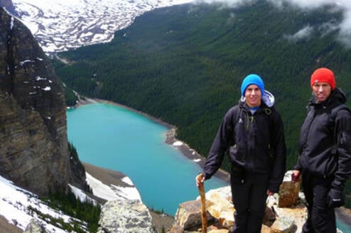 a girl stands on a ledge over looking a lake in the mountains
