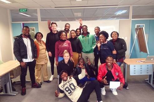 15 Students standing in front of a white board looking happy