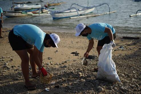 Two people cleaning up trash on a beach.