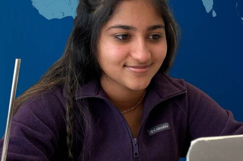 young woman smiling at computer with glass of water and a straw beside her and a virtual world behind her