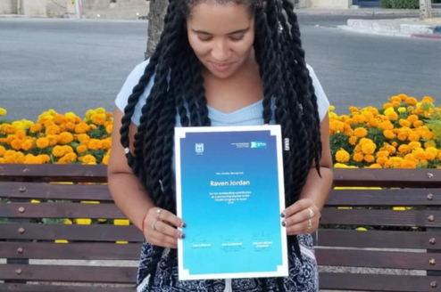 Woman with long black twists looking down at a certificate she's holding up to the camera