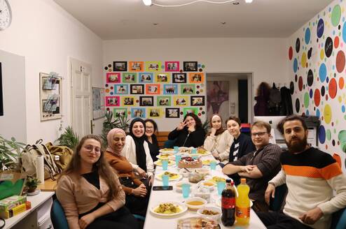 A large group poses for a photo while sitting around a table with food on their plates.