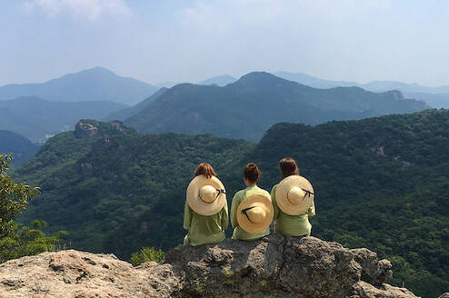 Three students sitting at the top of a mountain overlooking mountains in the distance