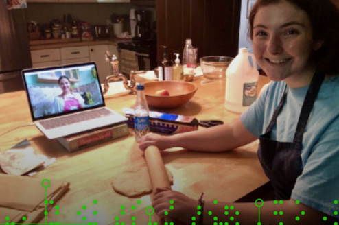 Image of a student with a rolling pin. A laptop in the background shows another student's face. 