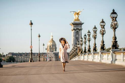 Woman wearing a hat walks across a bridge in Paris.