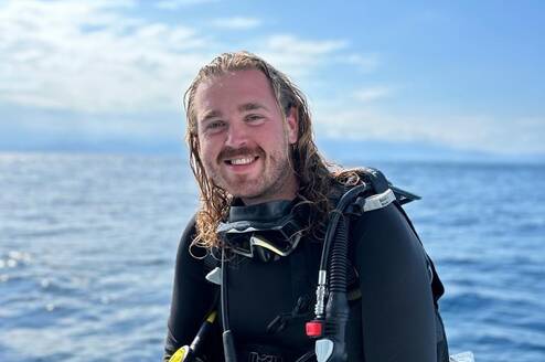 A happy male diver sitting on the edge of the dive boat in full gear smiling at the camera