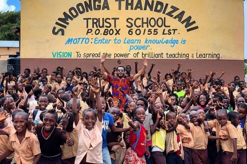Volunteer cheering with children outside Simoonga. 