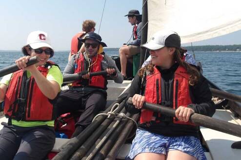 Students in a sailboat maneuvering oars.