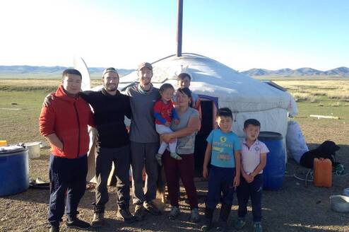 Volunteers and nomads are standing in front of the Mongolian traditional dwelling.