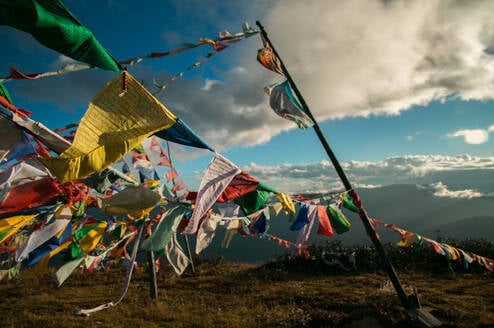 Prayer flags flying in the wind in the mountains of Bhutan with large clouds above in a light blue sky