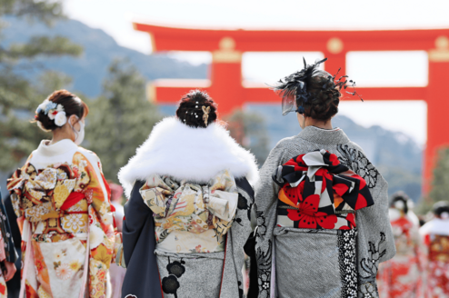 Traditional geisha walk towards a large torii gate in Japan