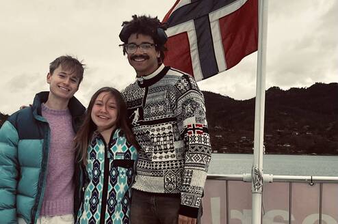 three college students stand smiling with the Norwegian flag waving in the wind