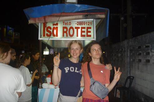 Two girls standing in front of a rotee street food cart 