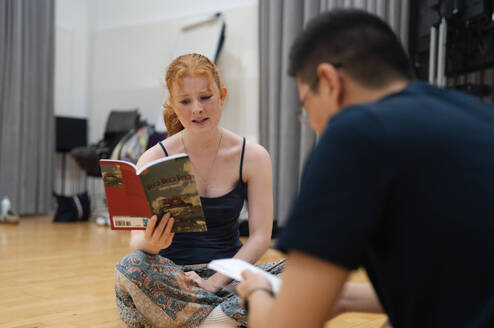 Two students sat in a hall reading scripts