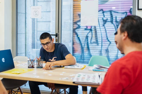 Students sitting around a table in a classroom, studying Spanish together with books and learning materials in a bright, modern setting.