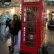 a student leaning against a red phone booth and smiling