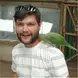 Andre van Dyk wearing a white and grey striped shirt, beard, and sunglasses with a green parrot on his shoulder