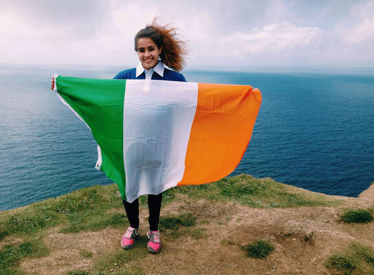 A student poses on a cliff with the Irish flag