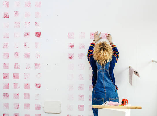 Student working on a piece of art, pink squares on a wall.