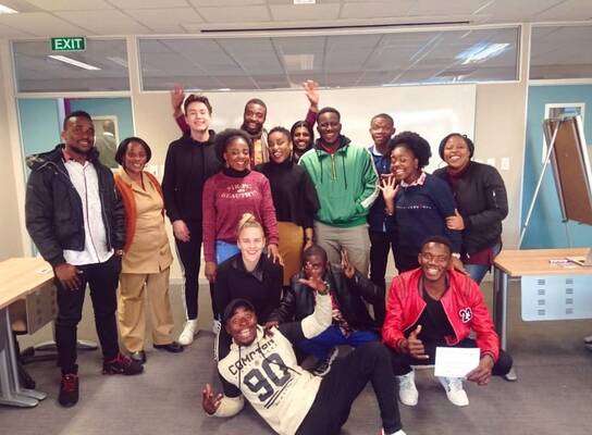 15 Students standing in front of a white board looking happy