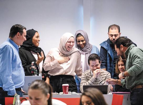 A group of male and female adults crowd around a laptop screen