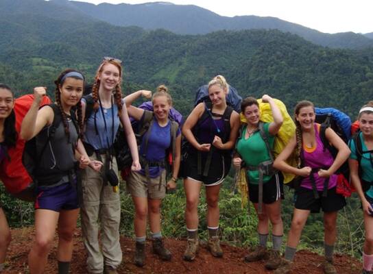 Crew poses for picture on a red dirt trail against background of lush mountain valley.