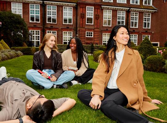 A group of students sitting on a green lawn smiling and talking.