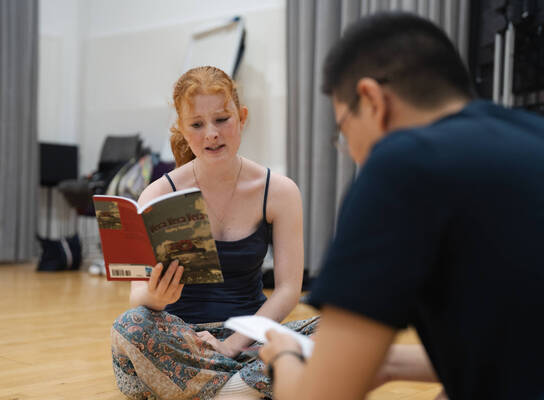 Two students sat in a hall reading scripts