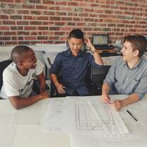 three boys laughing and talking at a table with design plans