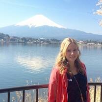 girl in a pink jacket smiling next to a lake with mountain in the background