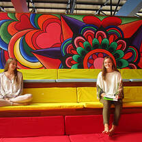 two girls on yellow couch in front of painted wall