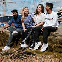 Four students sat on a wall laughing at Portsmouth Historic Dockyard
