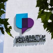 University of Portsmouth logo on the side of a university building through the trees
