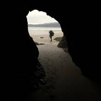 A student framed by a coastal cave on a NOLS Pacific Northwest backpacking expedition.