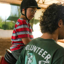 Projects Abroad Equine Therapy Intern assists a child as they ride a therapy horse