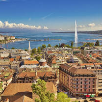Geneva skyline cityscape, French-Swiss in Switzerland. Aerial view of Jet d'eau fountain, Lake Leman, bay and harbor from the bell tower of Saint-Pierre Cathedral. Sunny day blue sky.