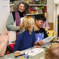A woman smiles at a child seated next to an NYU student