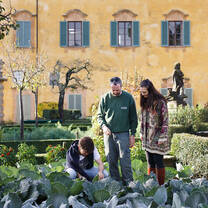A student crouches to garden while another student and gardener watch
