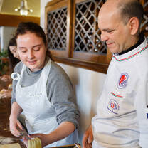 A student holds fresh made pasta in front of the cooking instructor