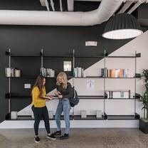 Two female students stand in front of bookshelves