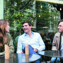 One female and two male postgraduate students sit at a table outside a cafe