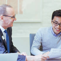 A male professor sits at a table next to a male student