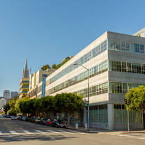 A large grey building lined with windows in San Francisco with the Transamerica Pyramid in the background