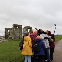 A group of students taking a selfie using a selfie stick in front of Stonehenge 