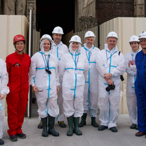 Students in full body red and white plastic suits and hard hats stand in a group and smile at the camera.