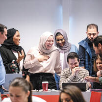A group of male and female adults crowd around a laptop screen